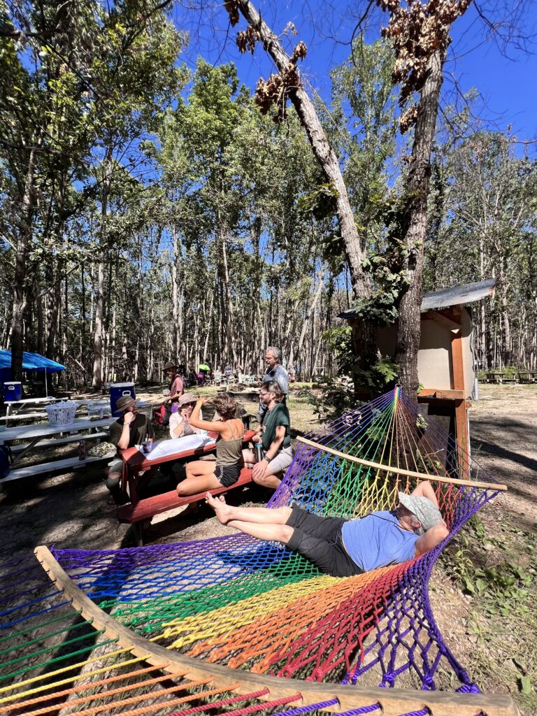 People sitting at a table and one person lounging in a hammock discussing their Working Group at the Convergence for Intentional Communities